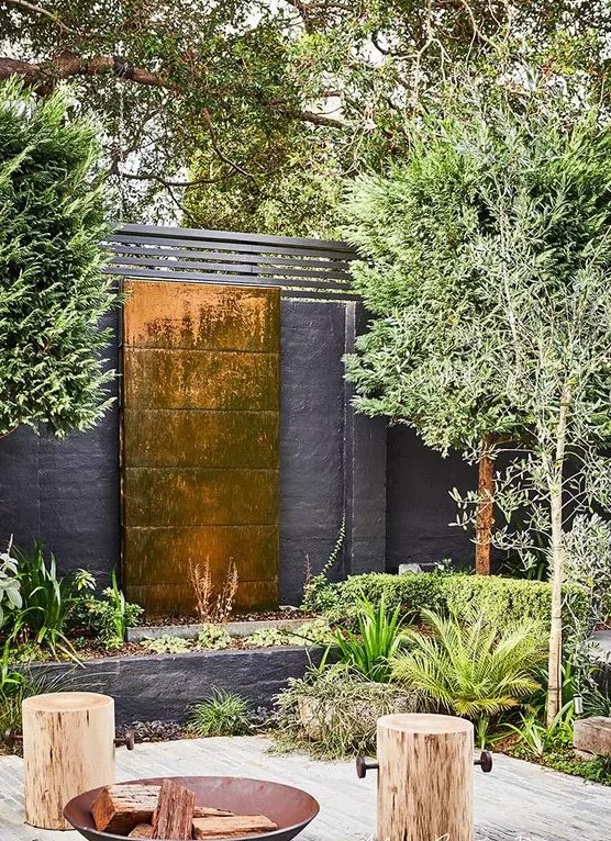 a lovely outdoor space with a copper waterfall, some greenery around, wooden stools and a metal fire bowl is amazing