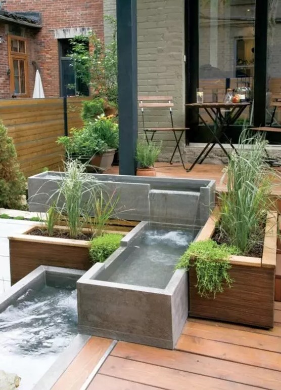 a modern outdoor space clad with a wooden deck, with a modern waterfall of concrete boxes and greenery is a cool and edgy nook
