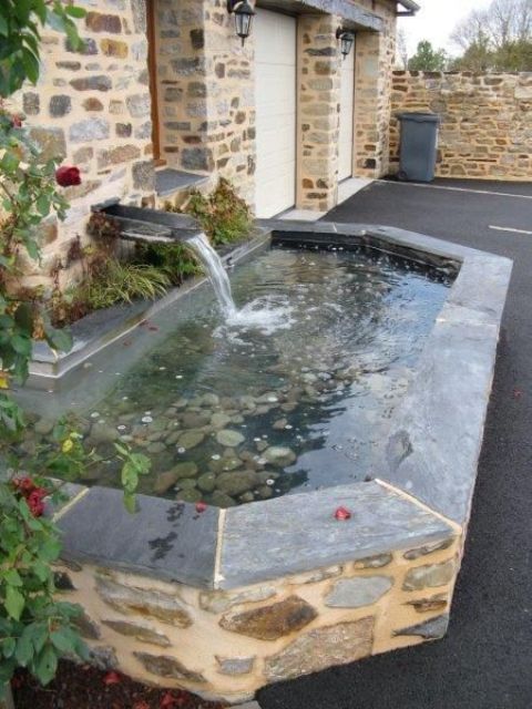 a modern pond with pebbles inside and stone borders plus a waterfall is a cool feature for an elegant garden