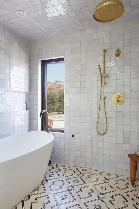 a neutral bathroom with white Zellige tiles and geometric ones, an oval tub and brass and gold fixtures