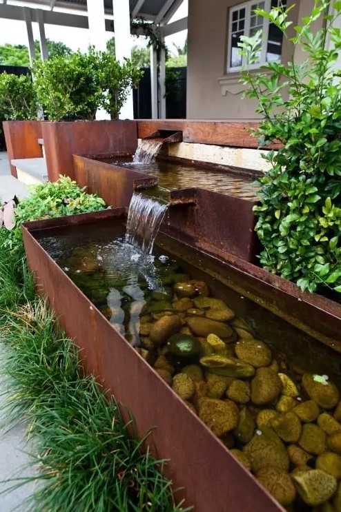 a modern waterfall with several faucets and bowls, with rocks inside and greenery around is a cool idea for a modern garden