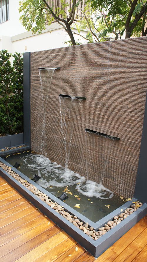 a stylish modern waterfal with a stone wall, a water feature and some rocks and pebbles around is a cool idea for a modern garden