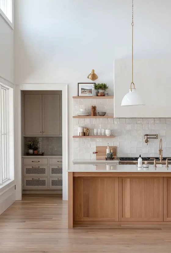 a sophisticated neutral kitchen with white and stained cabinets, a white zellige tile backsplash, a large hood and pendant lamps