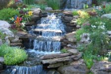 23 a beautiful garden waterfall with rocks placed on a slope, with greenery and bold blooms around is amazing