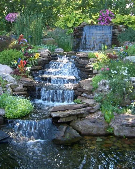 a beautiful garden waterfall with rocks placed on a slope, with greenery and bold blooms around is amazing