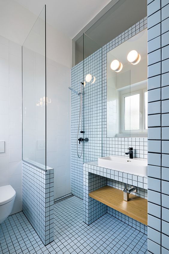 a blue bathroom clad with square tiles and with black grout, a tile clad vanity with a shelf, a mirror and a shower space