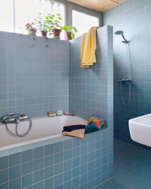 a blue bathroom clad with square tiles, with a shower and tub space, white appliances and potted greenery looks cool