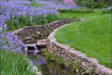24 a bold garden with a green lawn, purple and pink blooms and a waterfall clad with stone and bricks is wow