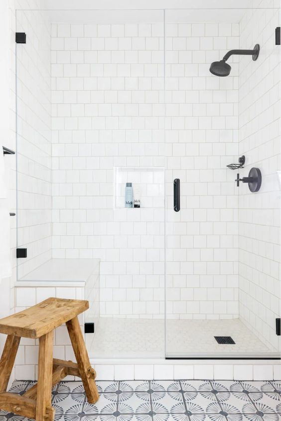 a catchy bathroom clad with white square and printed tiles, black fixtures for a more modern look and a wooden stool