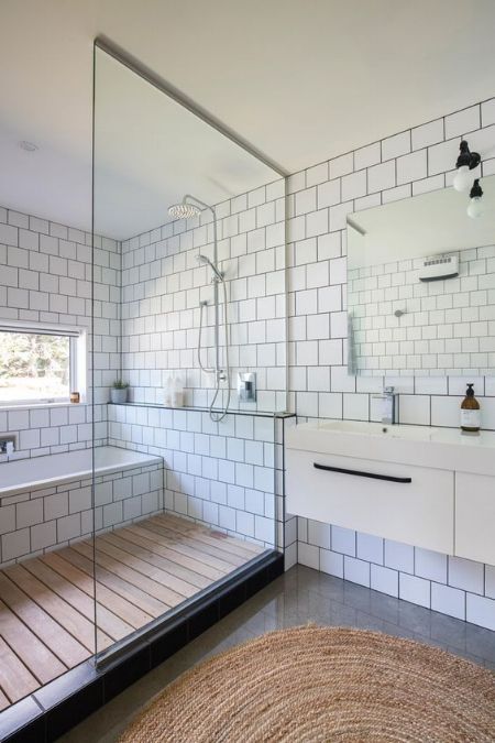 a catchy modern bathroom clad with white square tiles, with a large shower and tub space, a wooden floor there and a floating vanity