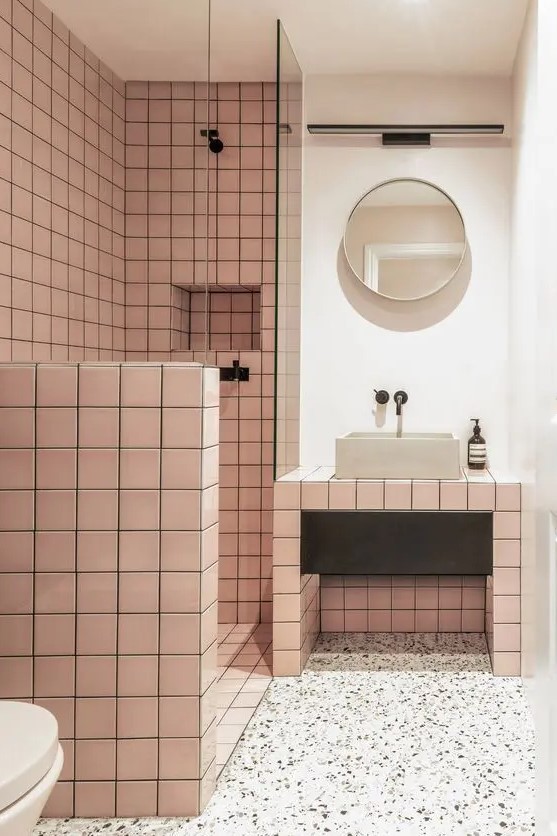 a catchy modern bathroom with pink square tiles, a terrazzo floor, a vanity clad with tiles and a round mirror
