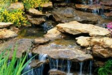 28 a cool backyard waterfall with rocks placed on a slope, with greenery and blooms is a lovely idea that feels Alpine