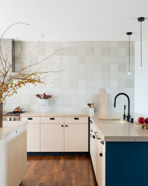 a cool modern kitchen with light stain and navy cabinets, stone countertops and grey square tiles on the wall