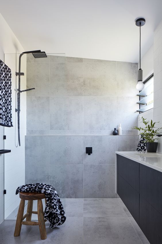 a contemporary bathroom clad with square grey tiles, with a navy vanity, a wooden stool and black fixtures