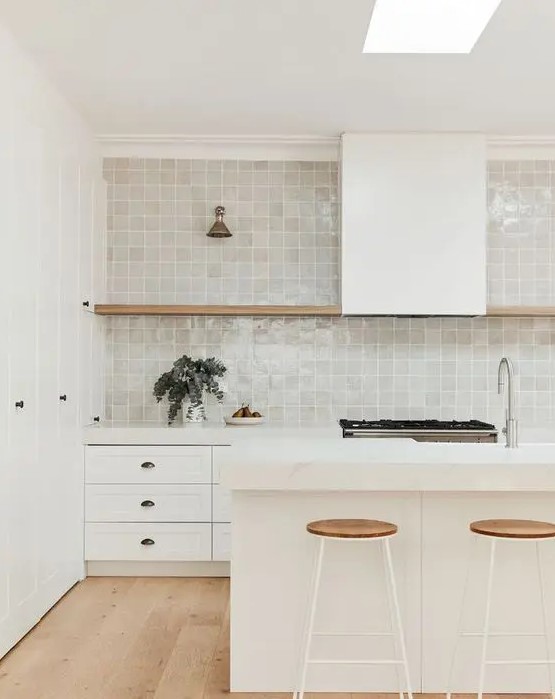 a creamy kitchen with shaker cabinets, a grey zellige tile backsplash, a hood and an open shelf