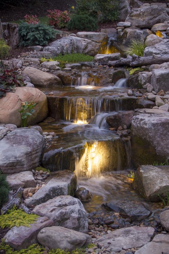 a descending waterfall clad with rocks and pebbles, with built-in lights and greenery and blooms is amazing