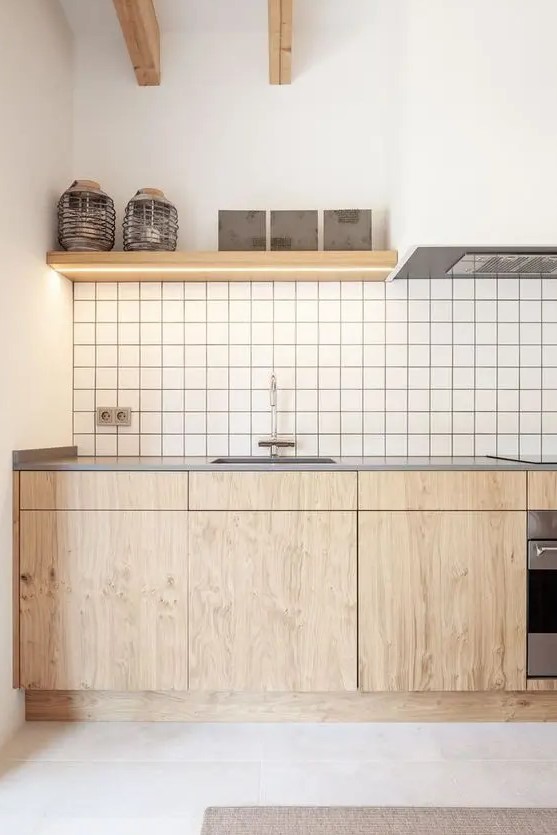 a lovely minimalist kitchen with stained lower cabinets, a white square tile backsplash, open shelves with lights