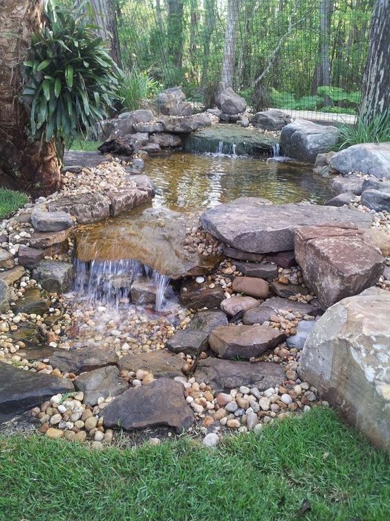 a green garden with trees and greenery, a waterfall composed of large rocks and smaller pebbles is a cool idea if you love natural looks