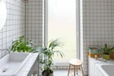 34 a light-filled bathroom with white square tiles, a tub clad with tiles, a vanity clad with them, too, some potted greenery