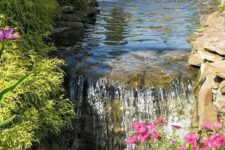35 a large garden with a pond that becomes a waterfall and flows into the next pond, with rocks, blooms and greenery around