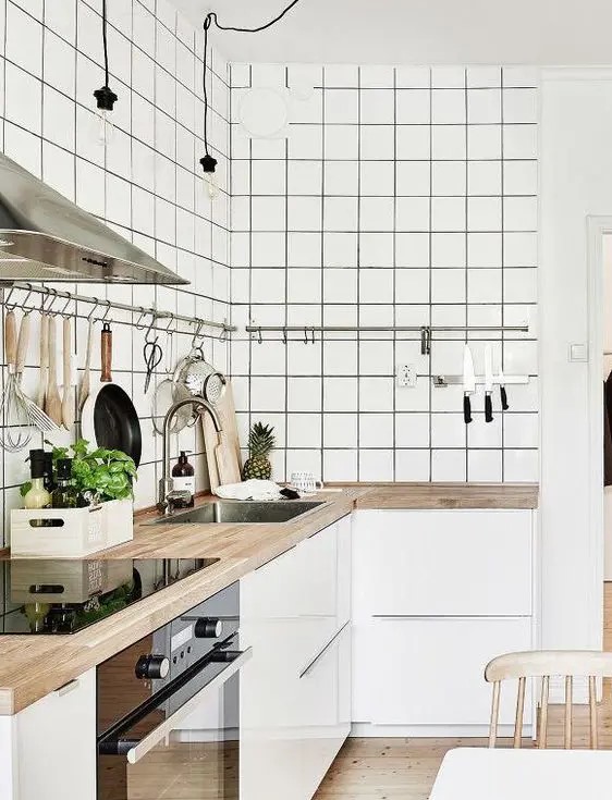 a minimalist white kitchen with sleek cabinets, white square tiles, butcherblock countertops and railings along the cabinets