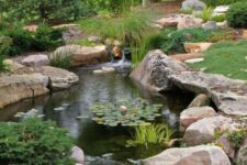 36 a large pond clad with rocks and greenery around and in the pond, with a waterfall clad with rocks is a lovely idea