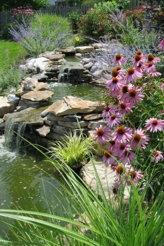 a lovely and natural-looking waterfall compsoed of rocks and with a sloping structure, surrounded with blooms and greenery