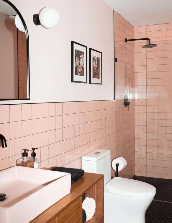 a modern bathroom clad with pink square tiles, with a shower, a stained vanity, white appliances and black fixtures