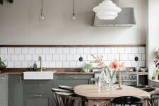 38 a Nordic kitchen with grey shaker cabinets, white square tiles, a stained table and black chairs, pendant lamps