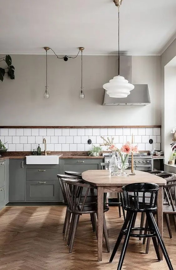 a Nordic kitchen with grey shaker cabinets, white square tiles, a stained table and black chairs, pendant lamps