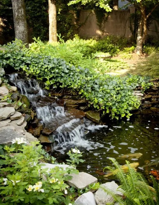 a lush garden with lots of greenery and a naturally styled descending waterfall that flows into a pond is a gorgeous space