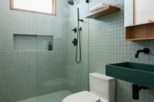 40 a modern bathroom with small scale square green tiles, a dark green sink, a mirror cabinet and black fixtures
