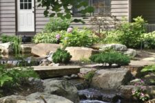 40 a natural backyard with rocks and pebbles, greenery and blooms and a waterfall that is descending down