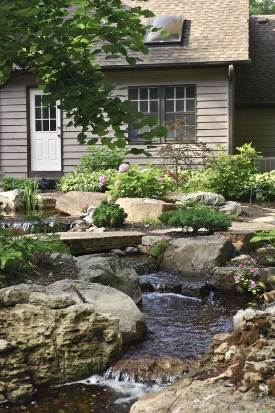 a natural backyard with rocks and pebbles, greenery and blooms and a waterfall that is descending down