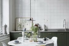 40 a pretty Nordic kitchen with dark green lower cabinets, white square tiles, a round table and white chairs and grey lamps