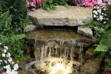 42 a natural-looking waterfall with large rocks and built-in lights plus white, pink and bold pink blooms around