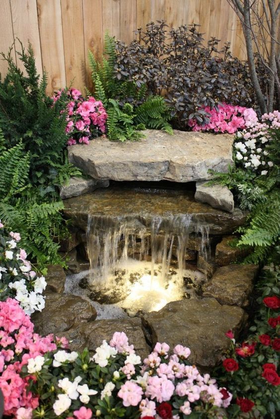 a natural-looking waterfall with large rocks and built-in lights plus white, pink and bold pink blooms around