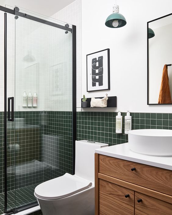 a modern bathroom with white walls and dark green square tiles, a stained vanity, a shower with black framing and pendant lamps