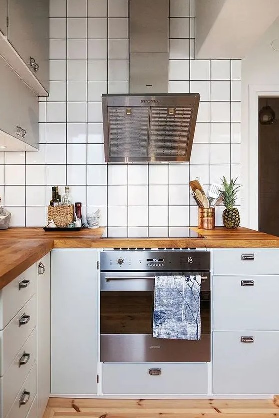 a Scandinavian kitchen with white cabinets, white square tiles on the walls, butcherblock countertops and stainless steel appliances