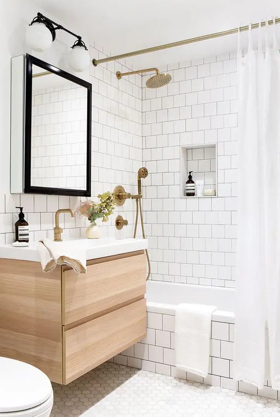 a neutral bathroom clad with white square tiles and hexagon ones, a tub clad with tiles, a timber vanity and brass fixtures