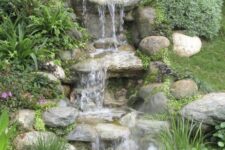 47 a rustic backyard waterfall with large rocks, greenery and blooms and a pond with green grass is a cool idea for a rustic garden