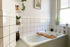 48 a neutral bathroom with a tub clad with green shiplap, white square tiles, a printed tile floor, potted plants and artwork