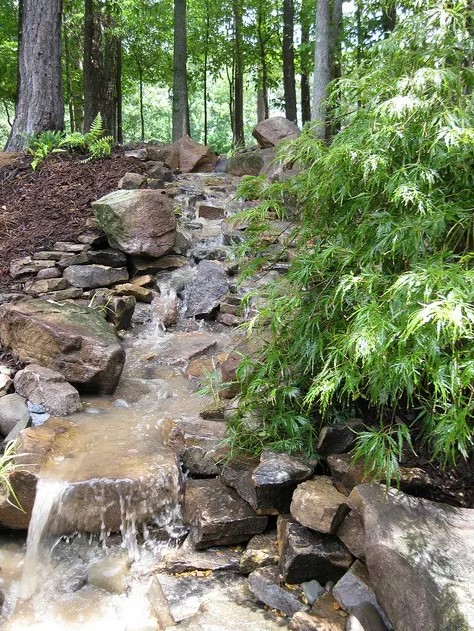 a sloping waterfall with rocks and greenery and trees around is a cool idea for any outdoor space, it looks natural