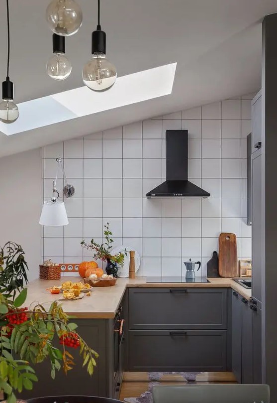 a small attic kitchen with graphite grey lower cabinets, a white square tile backsplash, a black hood and greenery