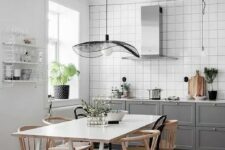 50 a stylish Scandinavian kitchen with white square tiles, grey shaker cabinets, a hood, a white table and stained chairs and a catchy pendant lamp