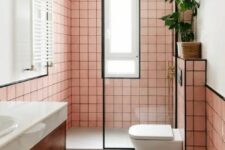 53 a pink bathroom clad with square tiles and black grout, black framing, a stained vanity and brass fixtures