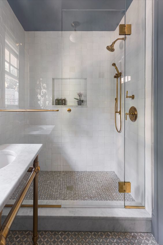 a refined bathroom with white square and printed tiles, white marble, elegant brass fixtures and a window
