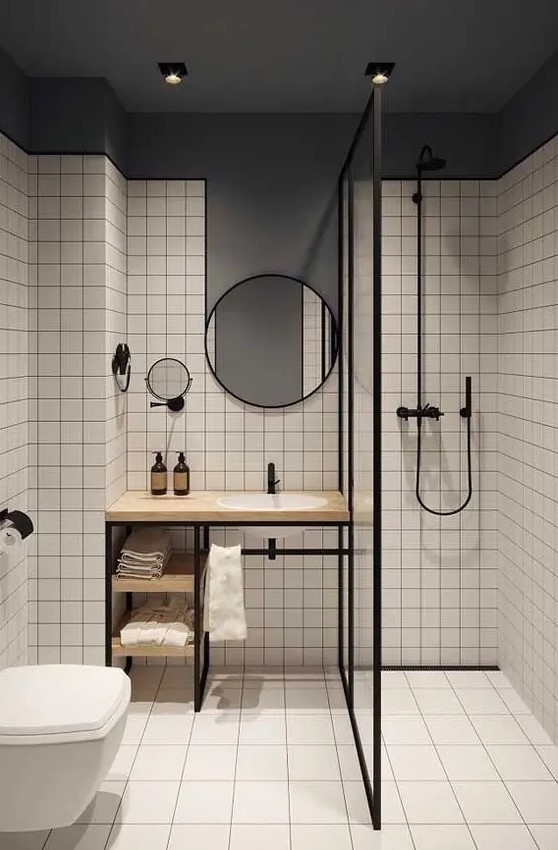 a stylish contrasting modern bathroom with white square tiles and a grey ceiling and wall, a shower, a vanity, round mirrors and black fixtures