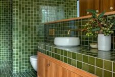 60 a welcoming bathroom with green square tiles and a stained floor and vanity, white applinaces and brass fixtures and a large mirror