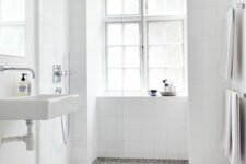 61 an airy Scandinavian bathroom with white square tiles and a terrazzo floor, a wall-mounted sink and stainless steel fixtures